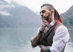 Stylish fashionable informal brutal man with dreadlocks, tattoos and piercings in a suit on nature