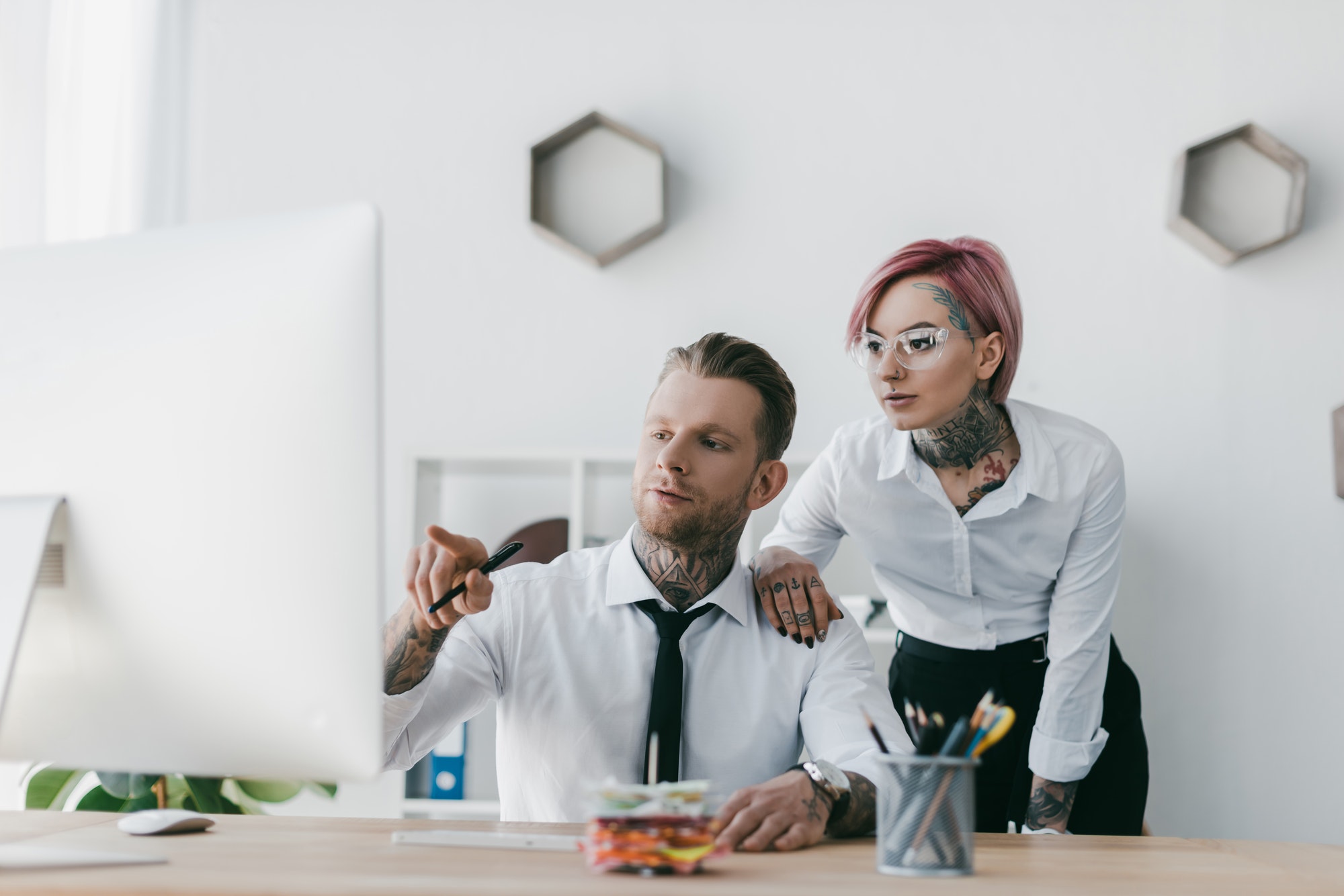 young tattooed business people looking at desktop computer in office